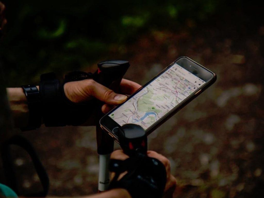A gloved hand holds a smartphone showing a street map above the handlebars of a bicycle.
